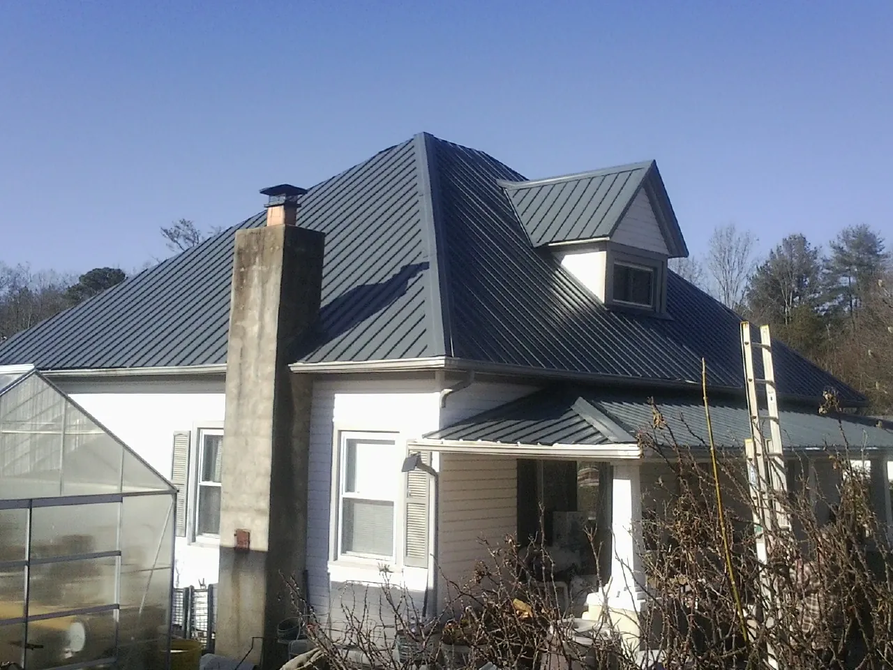 Dark blue standing seam metal roof on a white farmhouse with dormer — Slate & Tile Roof Repair by Roofing Brothers in North Freedom