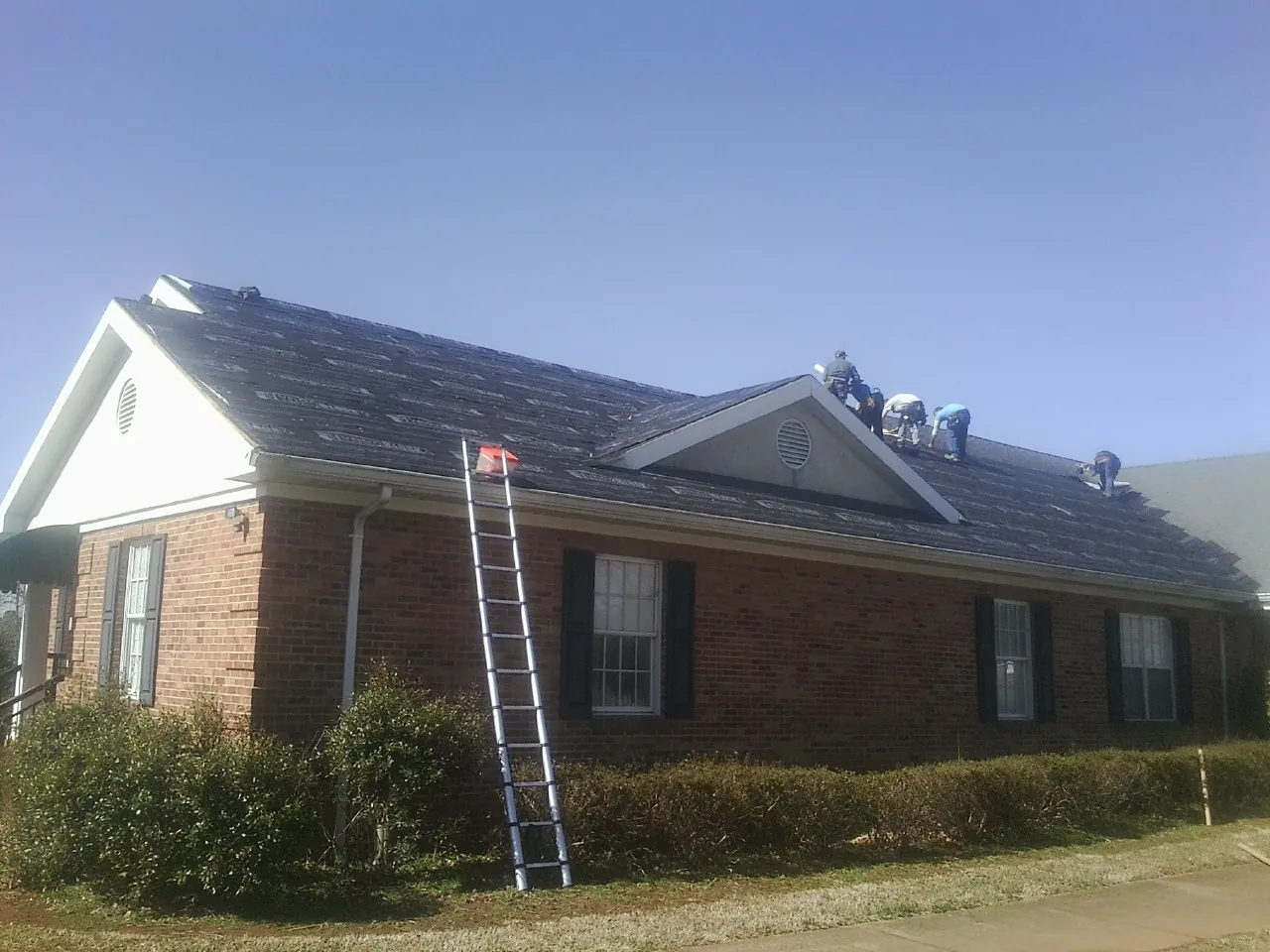 Crew tearing shingles off a brick ranch roof with a ladder set — Metal Roof Repair work by our crew in North Freedom