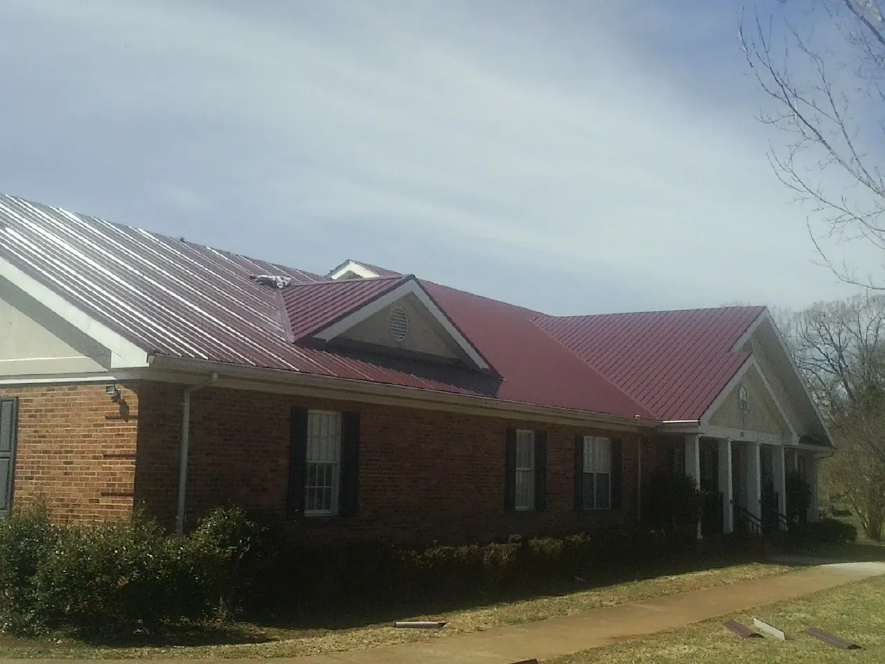 Red metal roof with gabled entries on a long brick building, from a Hail Damage Roof Repair job in North Freedom