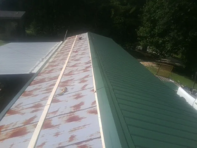Old rusted panels beside newly installed green metal roofing — Wind Damage Roof Repair by Roofing Brothers in North Freedom