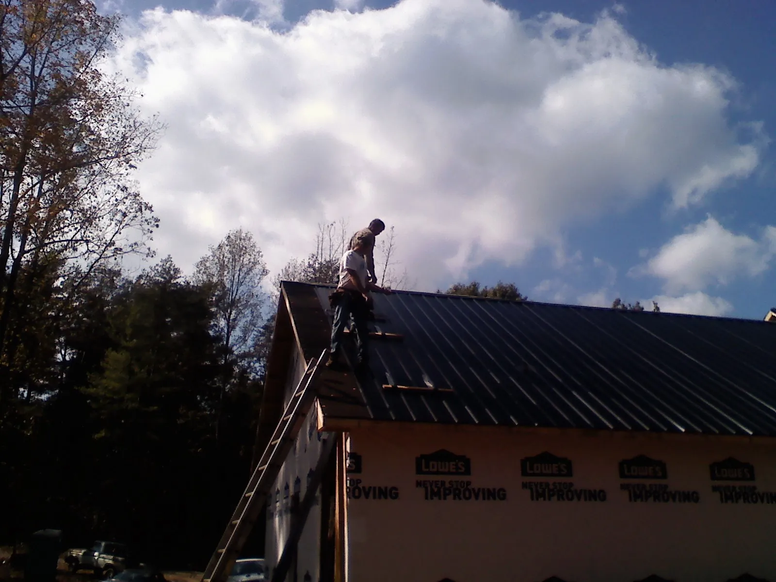 Roofer fastening dark metal panels high against a cloudy sky, from a Roof Inspection job in North Freedom