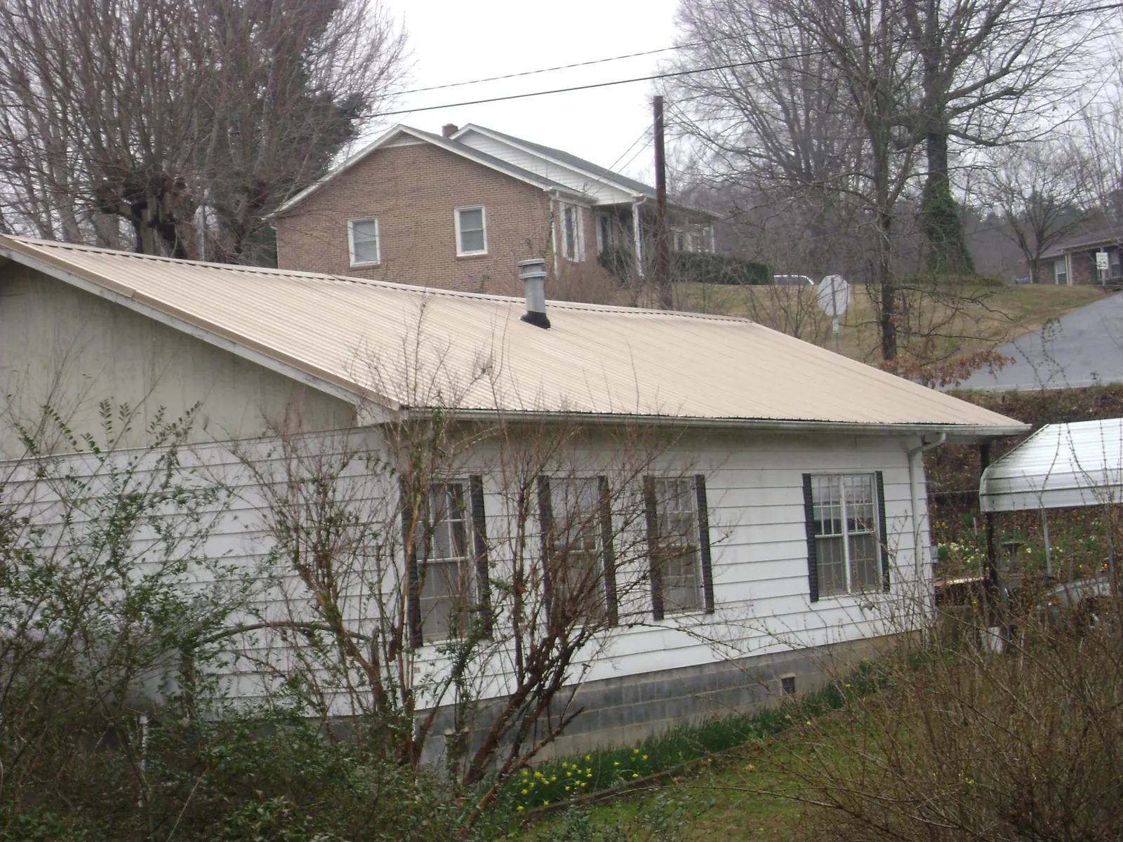 Tan metal roof on a white sided house set into a hillside — Commercial Roofing by Roofing Brothers in North Freedom
